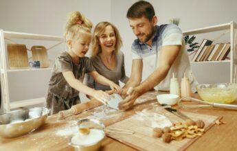 niña linda y sus hermosos padres preparando la masa para el pastel en la cocina de casa