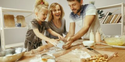 niña linda y sus hermosos padres preparando la masa para el pastel en la cocina de casa