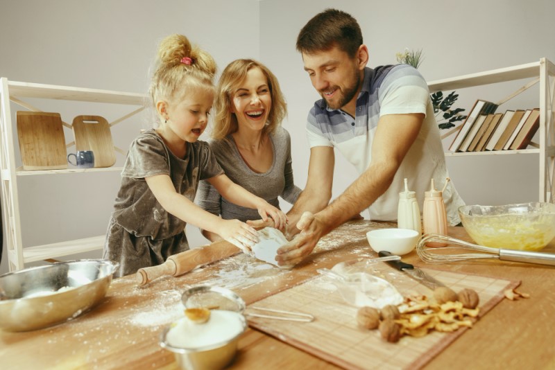 niña linda y sus hermosos padres preparando la masa para el pastel en la cocina de casa