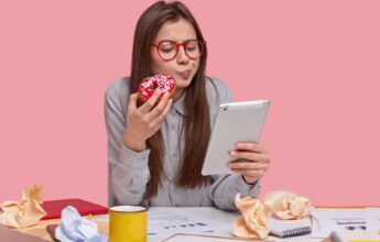 chica seria sostiene deliciosa rosquilla mientras trabaja con tablet