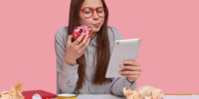 chica seria sostiene deliciosa rosquilla mientras trabaja con tablet