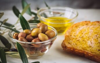 rebanadas de pan con aceite virgen extra cerca de tazones de vidrio llenos de aceite y aceitunas