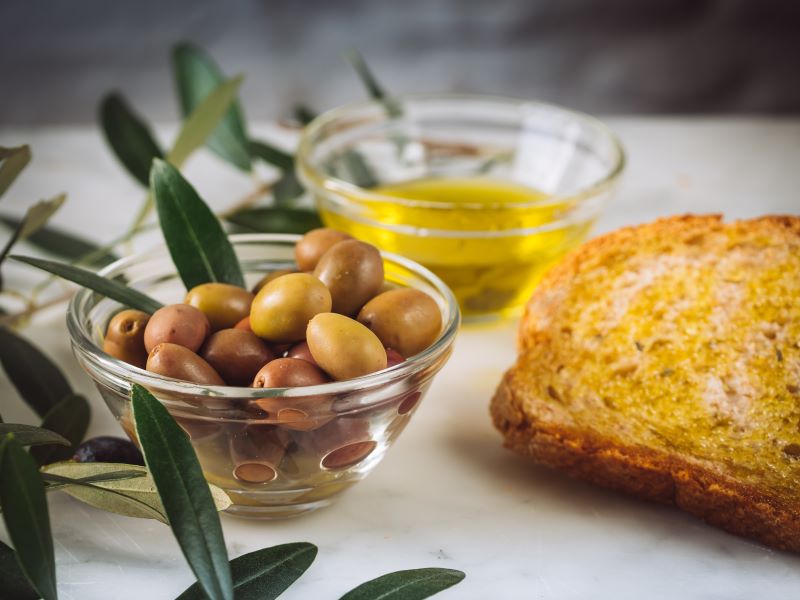 rebanadas de pan con aceite virgen extra cerca de tazones de vidrio llenos de aceite y aceitunas