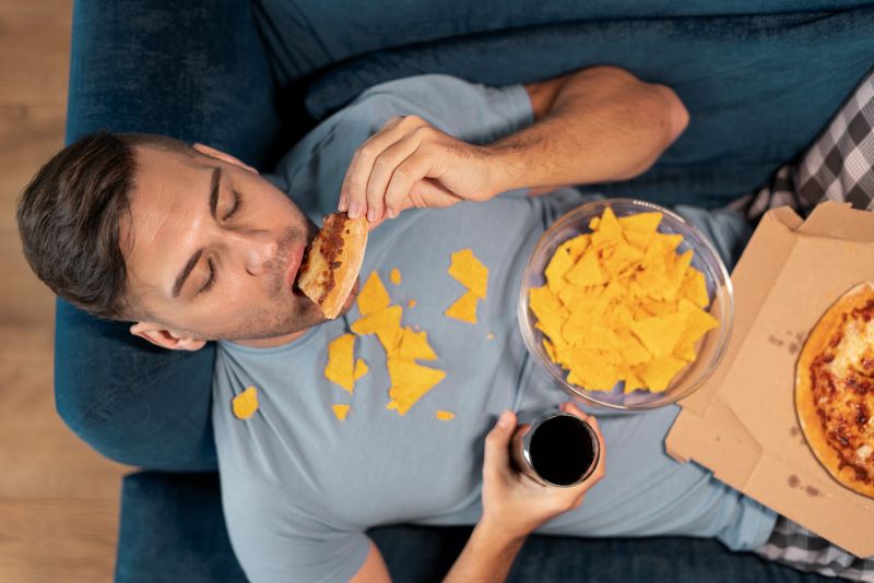 hombre tumbado en el sofa dandose un atracon de comida basura