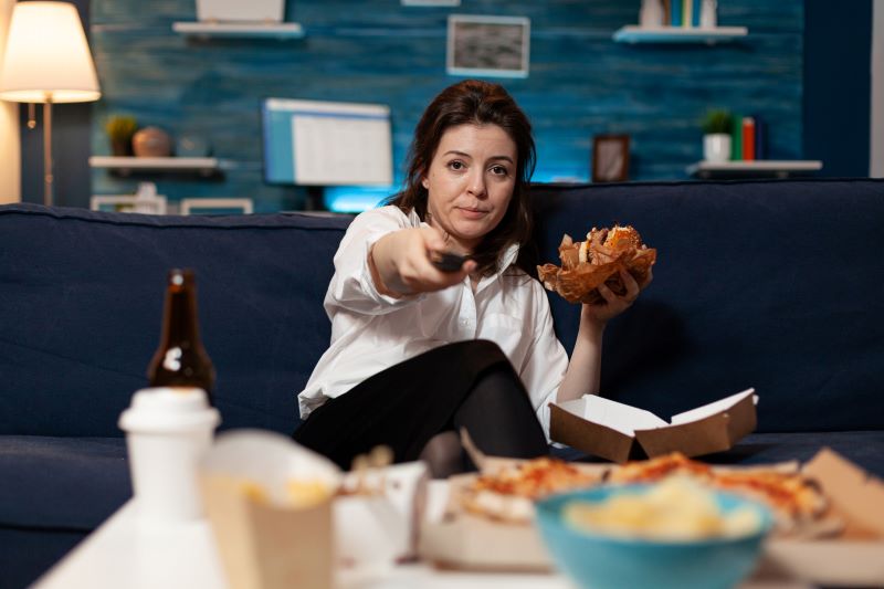 mujer cambiando de canal mientras come comida basura